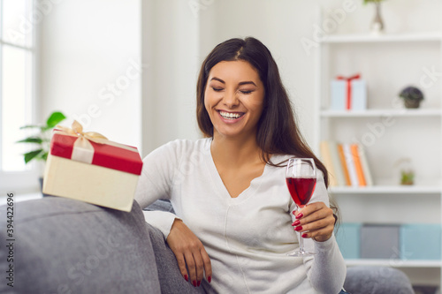 Laughing young woman holding glass of wine or champagne during online celebration videocall