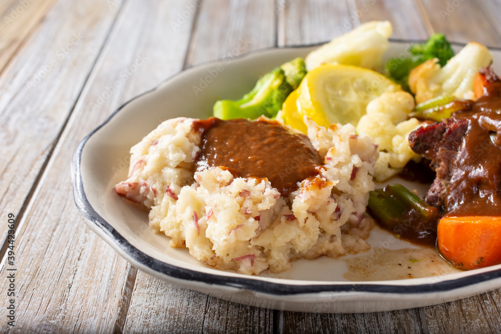 A view of a side of mashed potatoes, topped with gravy, part of a pot roast entree.