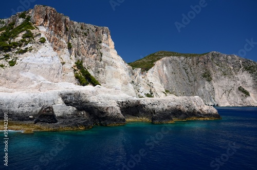Limestone rocks on the coast of Zakynthos island, Greece. Sunny day, crystal clear water, blue sky, boat trip, rocks falling steeply into the sea.