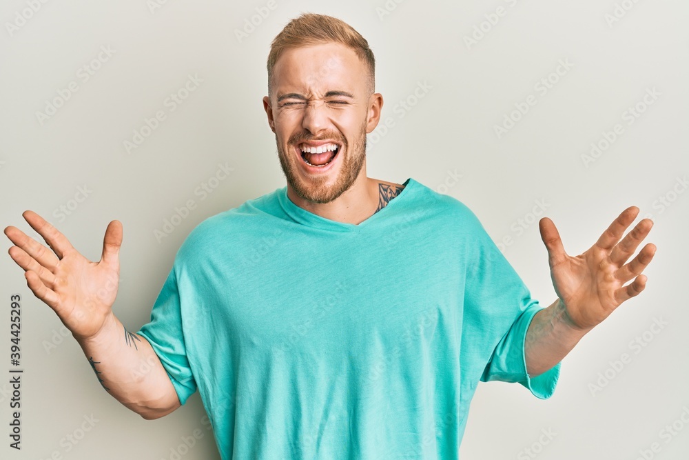 Young caucasian man wearing casual clothes celebrating mad and crazy for success with arms raised and closed eyes screaming excited. winner concept Young caucasian man wearing casual clothes celebrating mad and crazy for success with arms raised and closed eyes screaming excited. winner concept