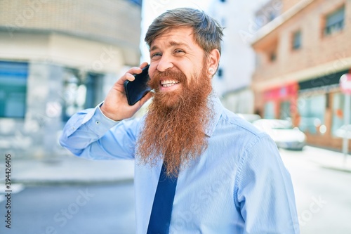 Young handsome redhead businessman smiling happy. Standing with smile on face having conversation talking on the smartphone at street of city.