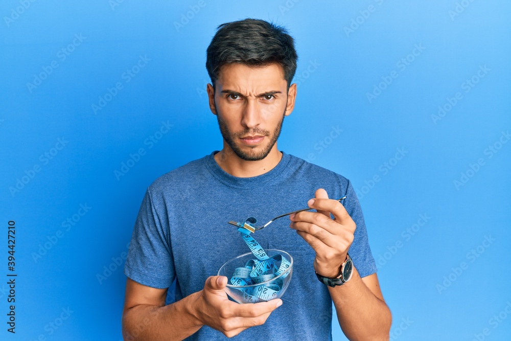 Young handsome man eating measure meter doing diet for weight loss skeptic and nervous, frowning upset because of problem. negative person. Young handsome man eating measure meter doing diet for weight loss skeptic and nervous, frowning upset because of problem. negative person.