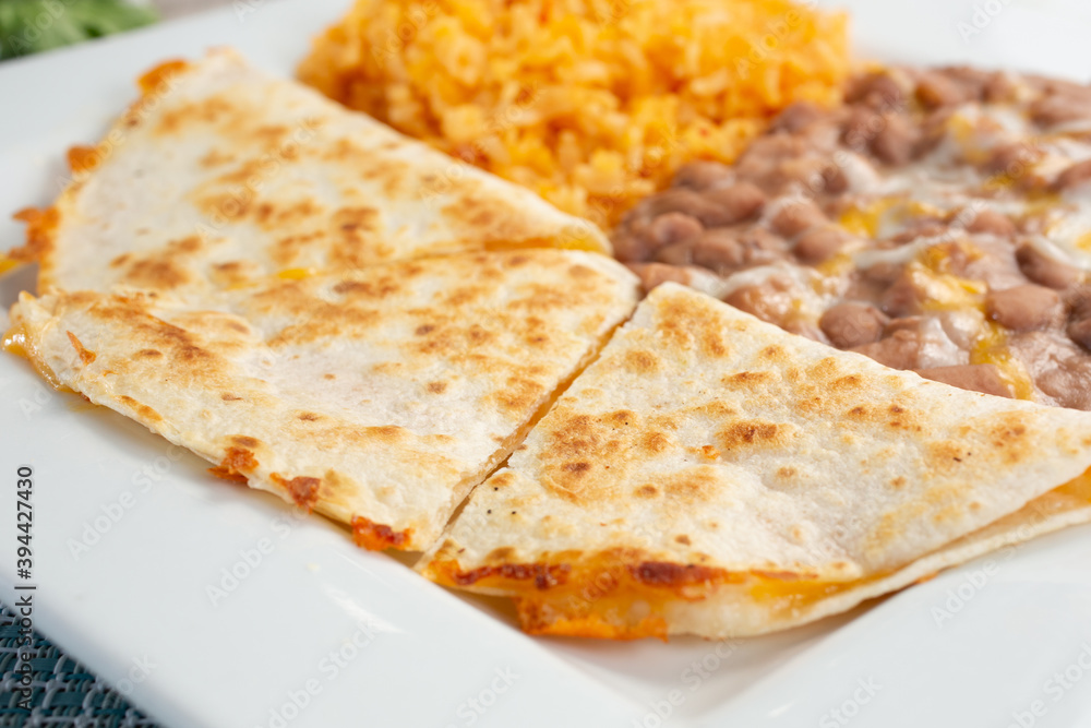 A view of a plate featuring a quesadilla, rice and beans, in a restaurant or kitchen setting.