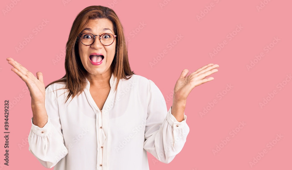 Middle age latin woman wearing casual clothes and glasses celebrating crazy and amazed for success with arms raised and open eyes screaming excited. winner concept Middle age latin woman wearing casual clothes and glasses celebrating crazy and amazed for success with arms raised and open eyes screaming excited. winner concept