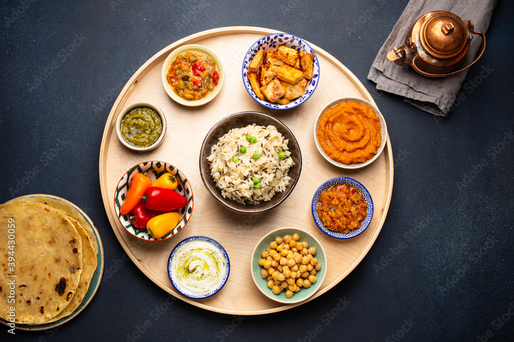Indian Thali - selection of various dishes served on round wooden platter. Assorted Indian vegetarian meze with boiled basmati rice, paneer, dal, chutney, chapati bread and brass teapot. Top view Indian Thali - selection of various dishes served on round wooden platter. Assorted Indian vegetarian meze with boiled basmati rice, paneer, dal, chutney, chapati bread and brass teapot. Top view