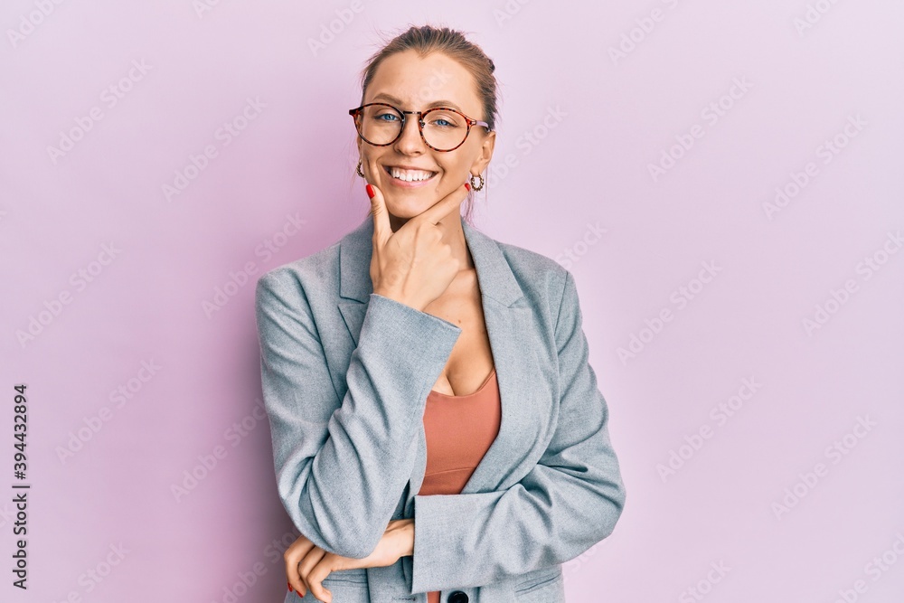Beautiful caucasian woman wearing business jacket and glasses looking confident at the camera smiling with crossed arms and hand raised on chin. thinking positive.