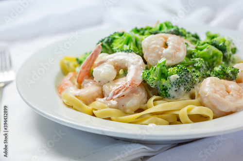 A view of a plate of broccoli shrimp Alfredo, in a restaurant or kitchen setting.
