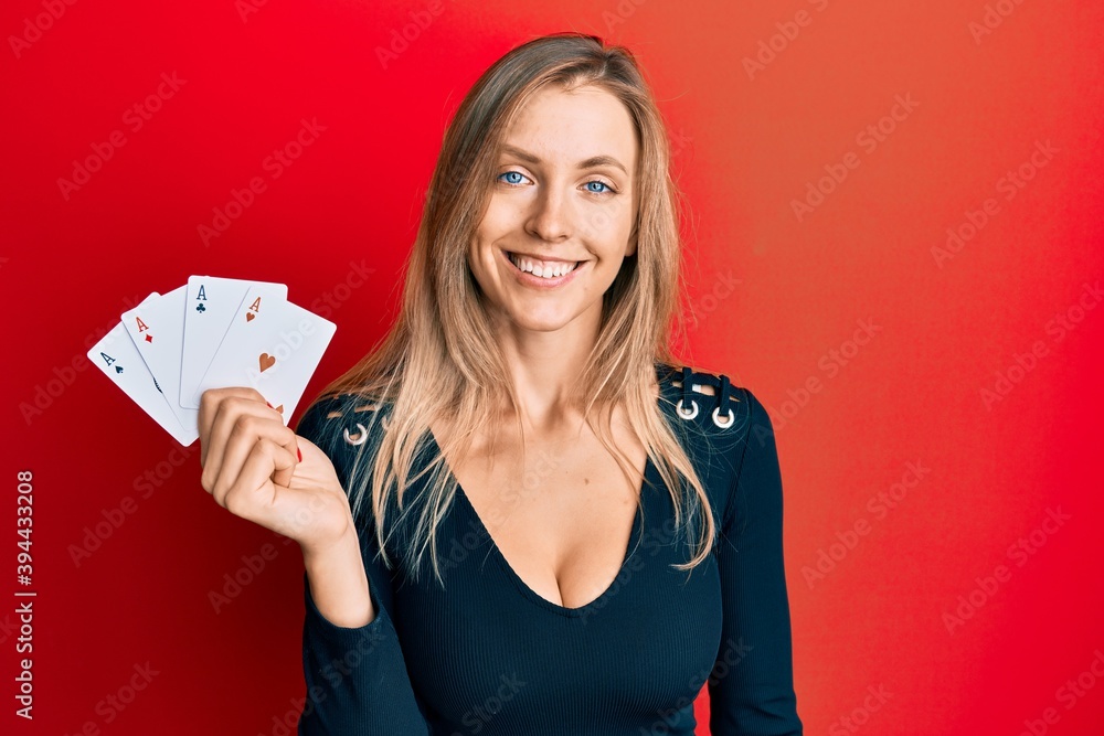 Beautiful caucasian woman holding ace poker cards looking positive and happy standing and smiling with a confident smile showing teeth Beautiful caucasian woman holding ace poker cards looking positive and happy standing and smiling with a confident smile showing teeth