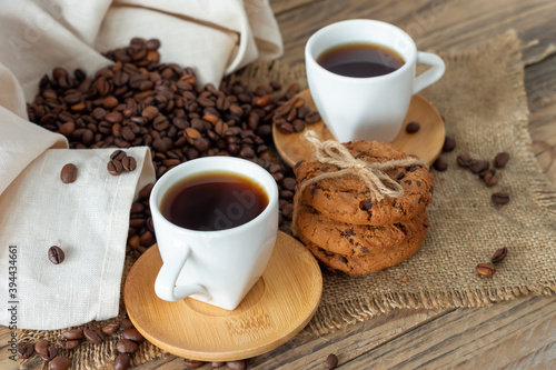 Two cups of freshly brewed espresso on wooden table. coffee beans and crunchie cookies on light wooden table, rustic style, homemade.