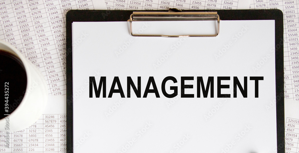 On the letter tablet is the text of MANAGEMENT, next to a mug of coffee and reports. On the letter tablet is the text of MANAGEMENT, next to a mug of coffee and reports.