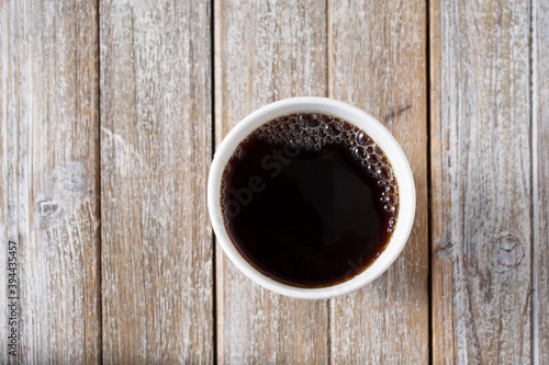 A top down view of a cup of coffee against a wood table surface.