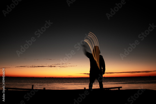 Human figure moving a light during sunset. Light painting on the edge of the river.