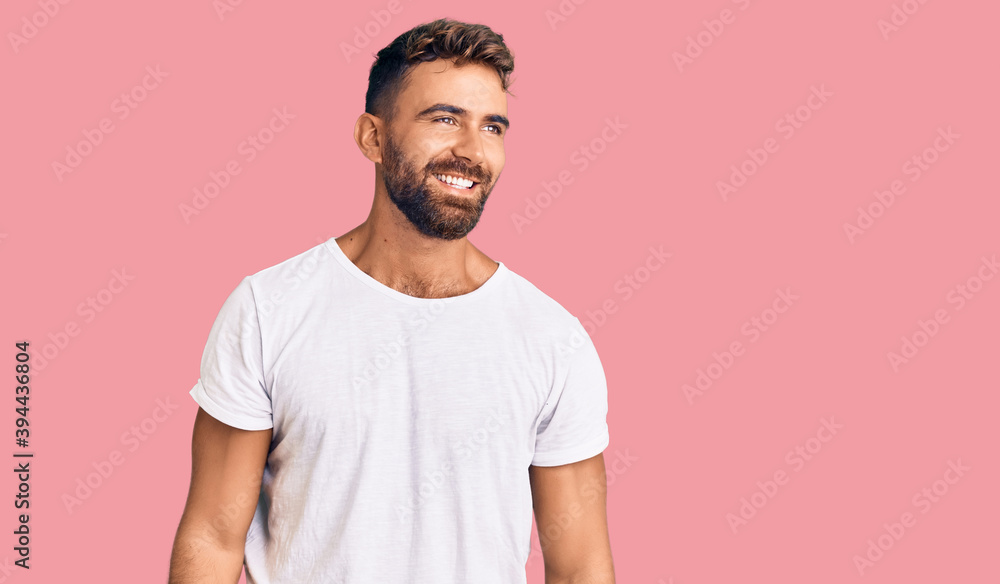 Young hispanic man wearing casual white tshirt looking away to side with smile on face, natural expression. laughing confident. Young hispanic man wearing casual white tshirt looking away to side with smile on face, natural expression. laughing confident.