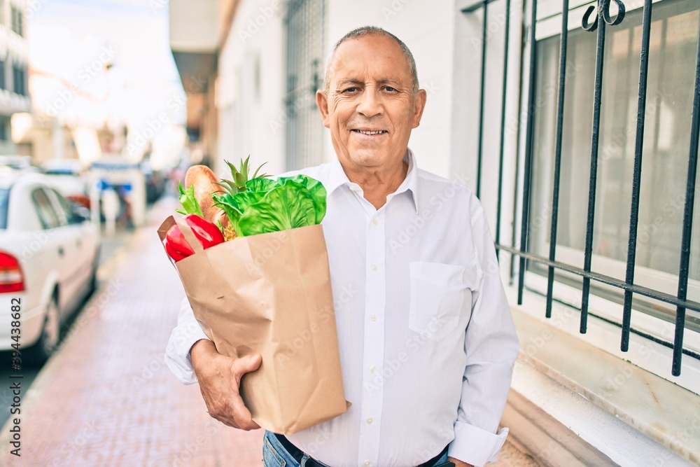 Senior man smiling happy holding paper bag with food walking at the city. Senior man smiling happy holding paper bag with food walking at the city.