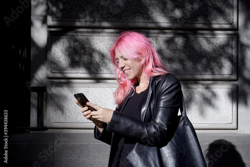 mujer vestida con abrigo de piel negro sonriendo mientras escribe un mensaje en su mobil photo