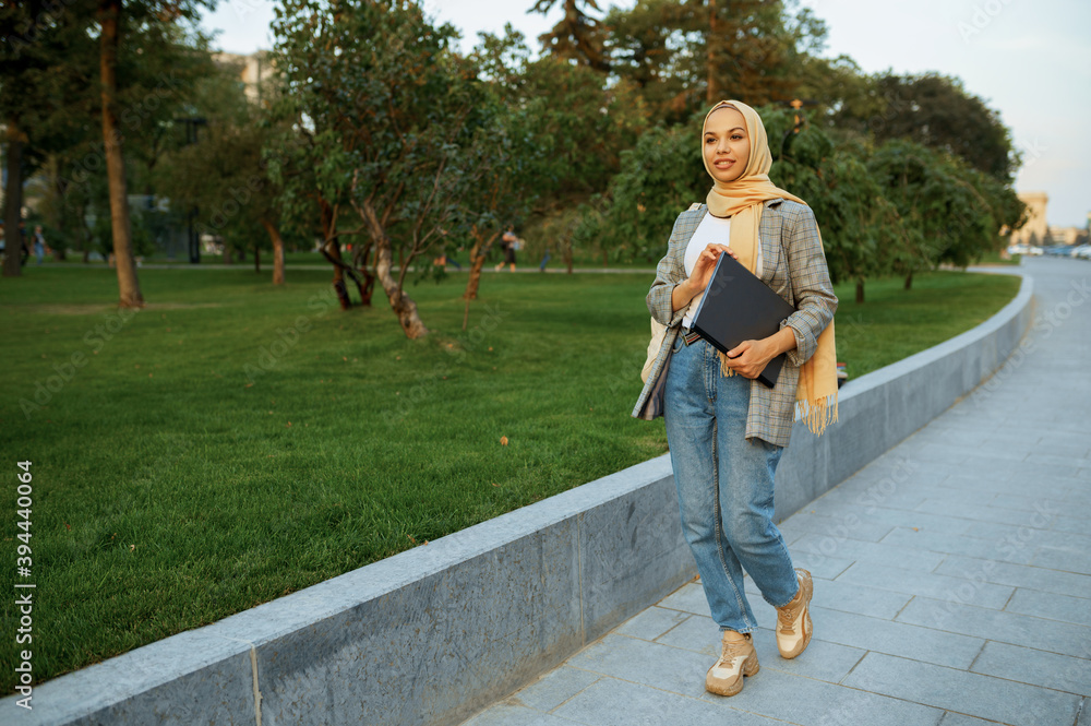 Arab female student with laptop walking in park