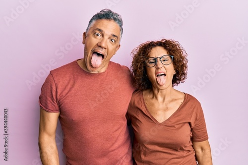 Beautiful middle age couple together wearing casual clothes sticking tongue out happy with funny expression. emotion concept.