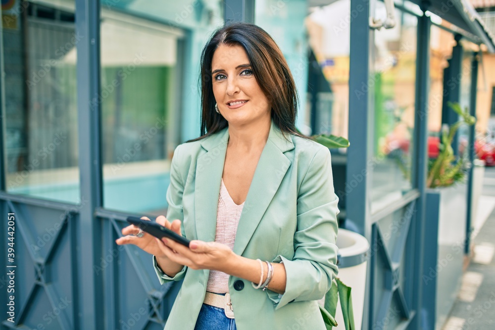 Confident business woman wearing elegant suit standing at the street using smartphone with cheerful face Confident business woman wearing elegant suit standing at the street using smartphone with cheerful face