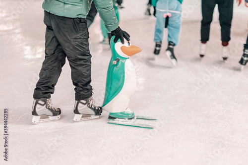Ice rink. Abstract boy holds a penguin for support and learning to skate outdoors in skating rink. Winter outdoor activities