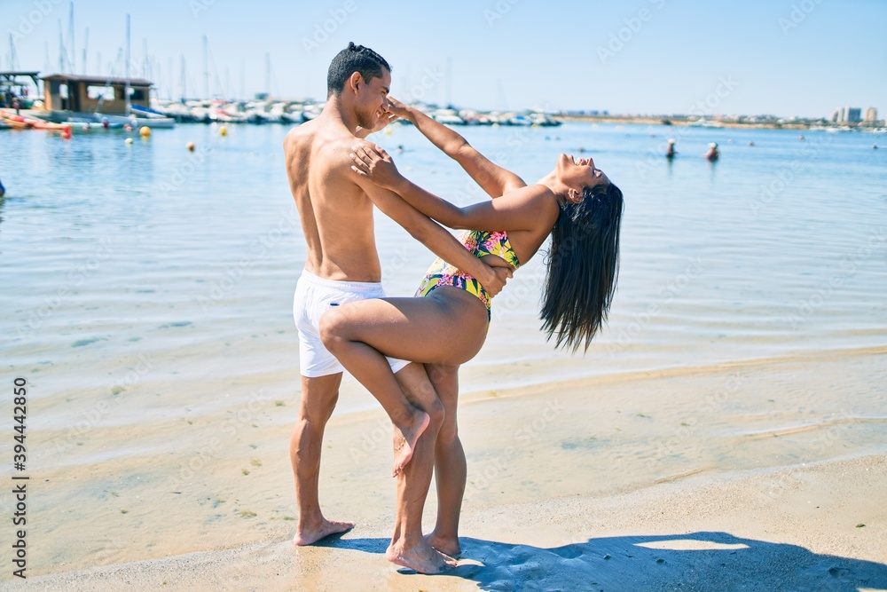 Naklejka premium Young latin couple wearing swimwear smiling happy and dancing at the beach.