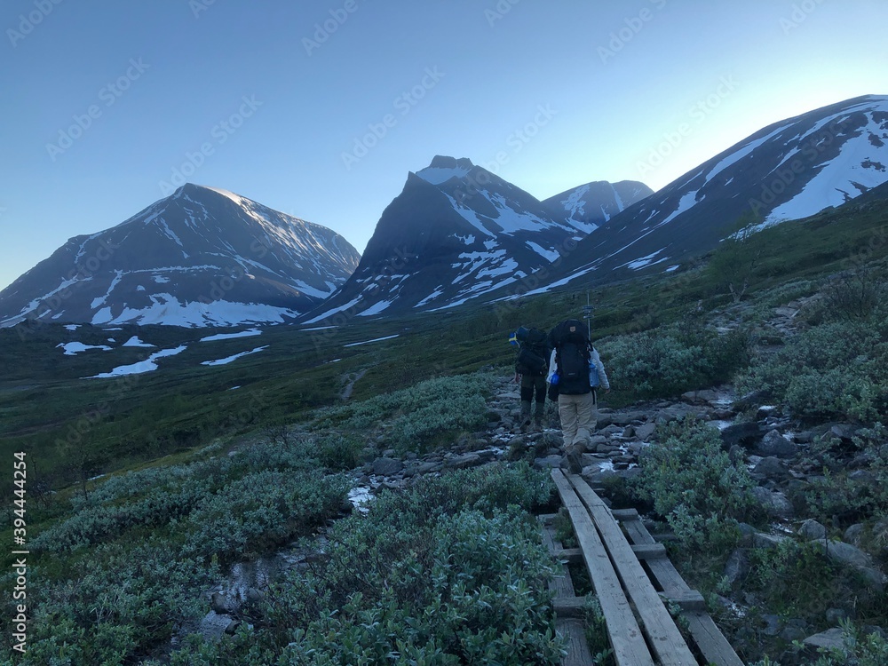 Hikers walking towards misty, snowy mountains in sunset
