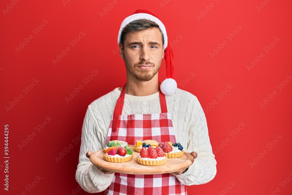Handsome caucasian man wearing baker apron and christmas hat holding cakes depressed and worry for distress, crying angry and afraid. sad expression. Handsome caucasian man wearing baker apron and christmas hat holding cakes depressed and worry for distress, crying angry and afraid. sad expression.