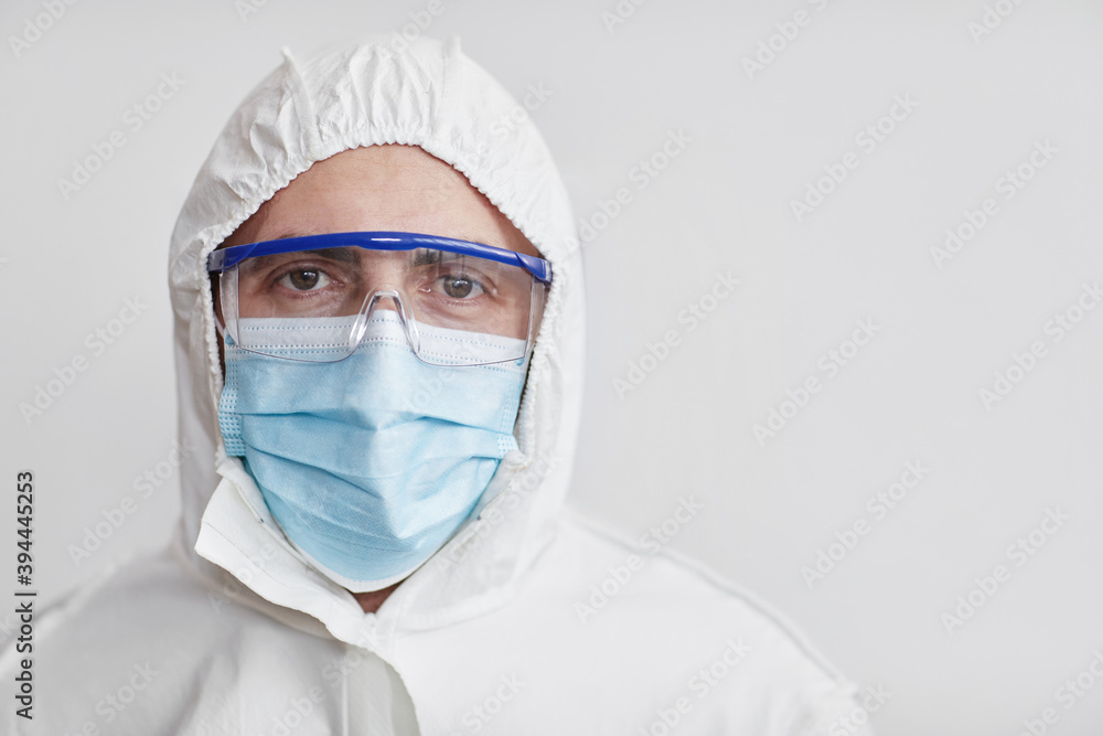 Close up portrait of male medical worker wearing full protective gear and looking at camera while posing against white background, copy space