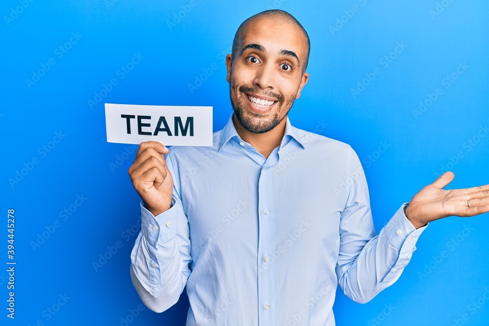 Hispanic adult business man holding team message on paper celebrating achievement with happy smile and winner expression with raised hand Hispanic adult business man holding team message on paper celebrating achievement with happy smile and winner expression with raised hand