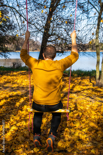 Photo of a young blonde woman on a swing in the middle of the woods in an autumn day. Vilnius.