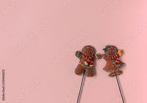 two gingerbread men a girl and a boy in Christmas clothes lie on a pink background