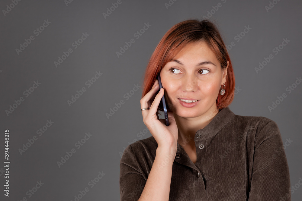 Beautiful woman is standing on a gray background and talking on the phone Beautiful woman is standing on a gray background and talking on the phone