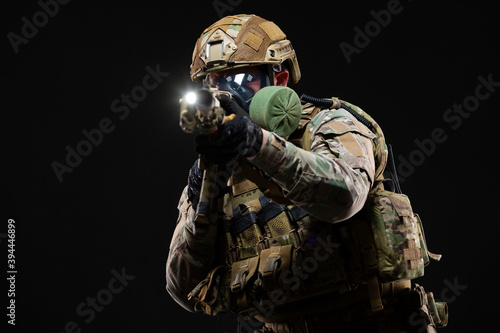 Military man in camouflage and in full combat readiness, wearing a helmet and gas mask, aims through a collimator sight directly at the enemy using chemical weapons isolated on black background