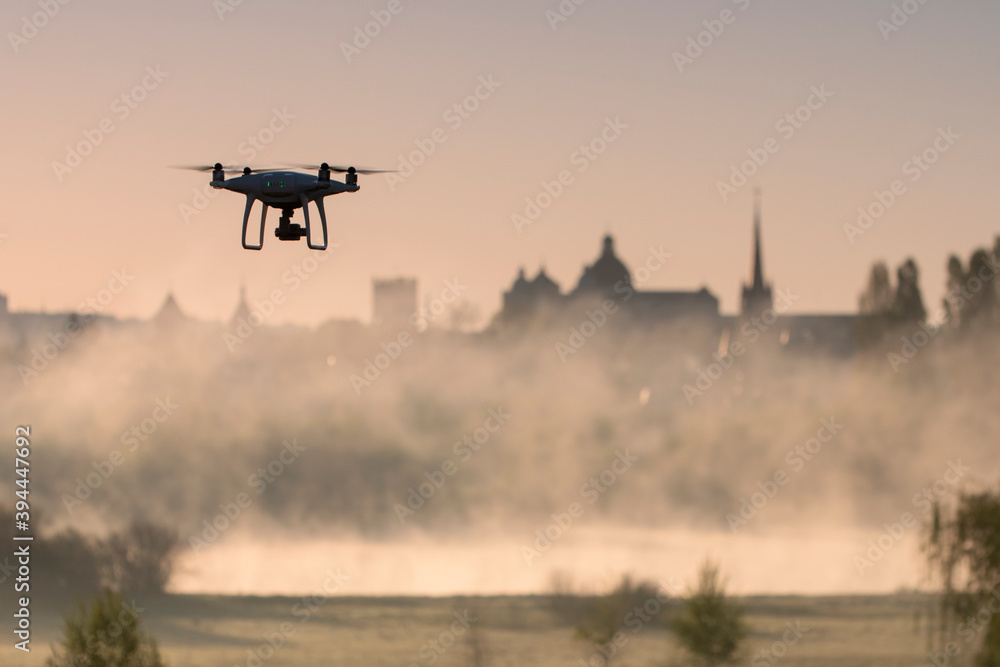 Fototapeta premium Quadcopter in flight on the background of the architecture of the old city of Lutsk (Ukraine) and the fog over the river Styr. Morning.