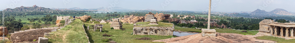 Hampi, Karnataka, India - November 4, 2013: Panorama shot from Sunset Hill over landscape filled with ancient temples and ruins in front of green agricultural land and hills on horizon under light blu