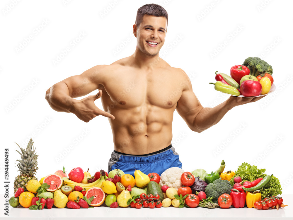 Obraz premium Topless male fitnes model posing with a plate of fruits and vegetables and pointing at his abs