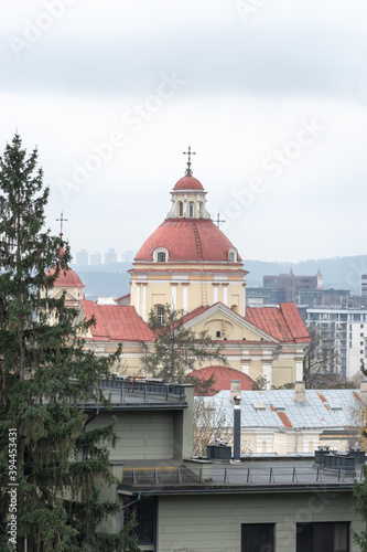 The upper part of Peter and Paul Church in Vilnius, the capital of Lithuania, on a foggy autumn day. In the background-new residential buildings. In the foreground-the roofs of the houses. Copy space