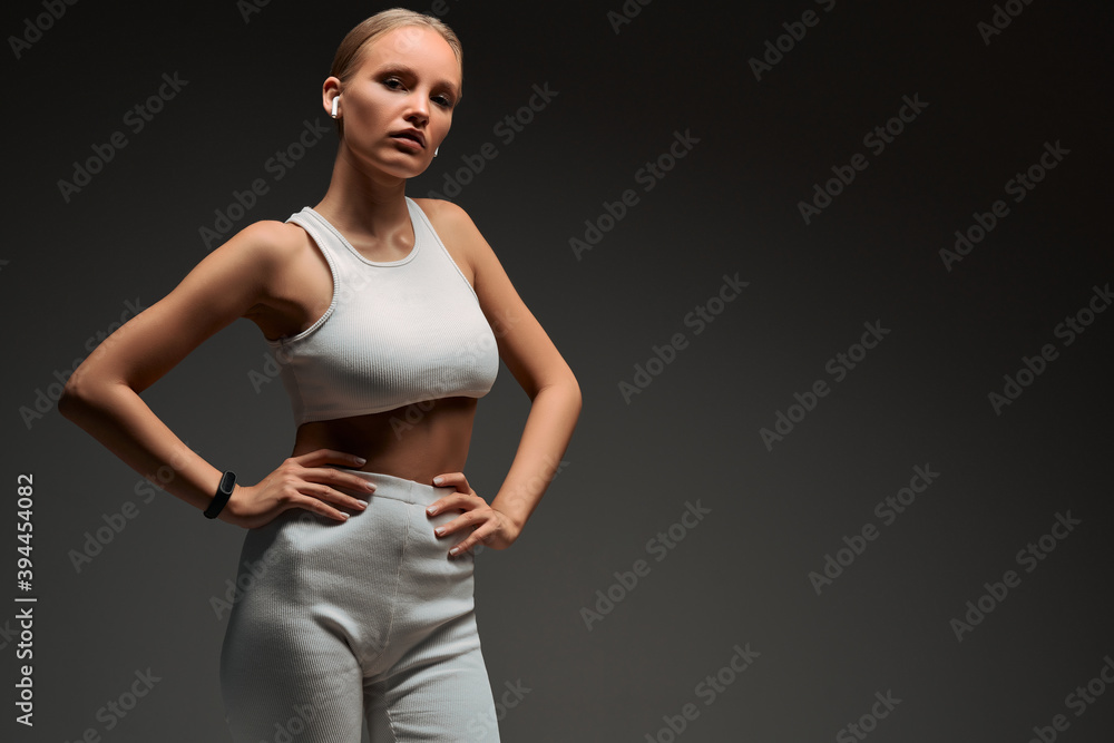 Sports blonde girl in white training clothes with headphones in the studio on a grey background. Sports blonde girl in white training clothes with headphones in the studio on a grey background.