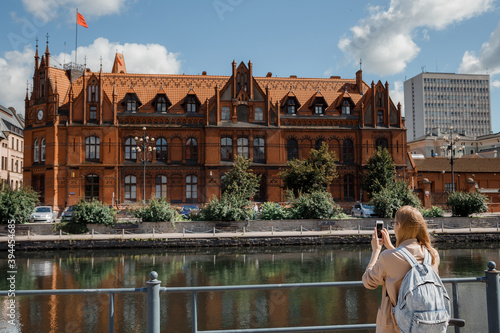 Young woman takes pictures of a beautiful building. House on the river. The girl with a backpack travels. Bydgoszcz. House of the Polish Post in Bydgoszcz photo