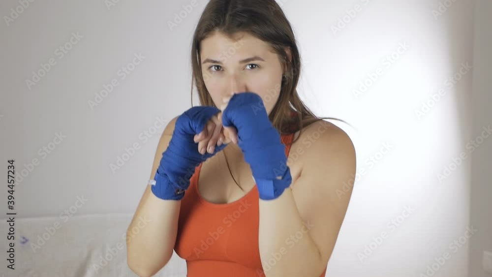 Front view of a muscular girl with sports bandages on her arms doing boxing workout. Young sportswoman workout movement. Sport concept, boxing Front view of a muscular girl with sports bandages on her arms doing boxing workout. Young sportswoman workout movement. Sport concept, boxing