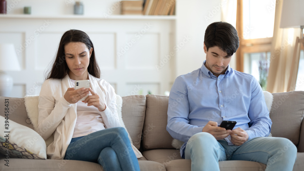 Substitute for real life. Focused young male and female spouses or friends sitting on sofa in silence ignoring one another spending time online looking at smartphone screens having internet addiction Substitute for real life. Focused young male and female spouses or friends sitting on sofa in silence ignoring one another spending time online looking at smartphone screens having internet addiction
