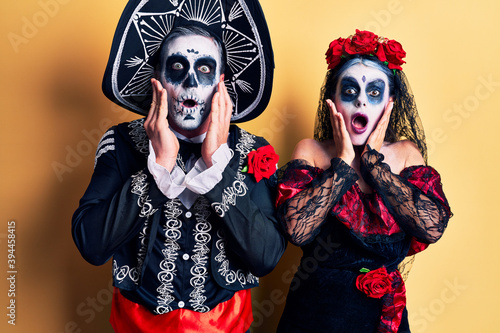 Young couple wearing mexican day of the dead costume over yellow afraid and shocked, surprise and amazed expression with hands on face