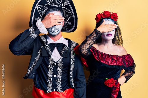 Young couple wearing mexican day of the dead costume over yellow covering eyes with hand, looking serious and sad. sightless, hiding and rejection concept