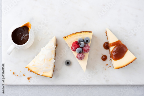 Assortment of cheesecakes with different toppings. Coconut cheesecake, caramel sauce cheesecake and slice of new york cheesecake with frozen berries. Top view photo