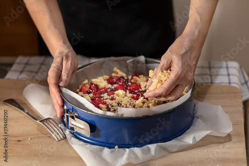 Hands putting crumble dough on a uncooked pie.