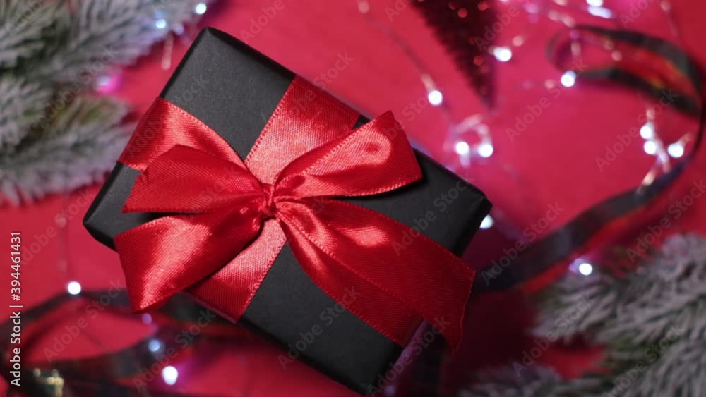 gift black box with red ribbon on top of christmas tree decorations with bokeh lights. gift black box with red ribbon on top of christmas tree decorations with bokeh lights.