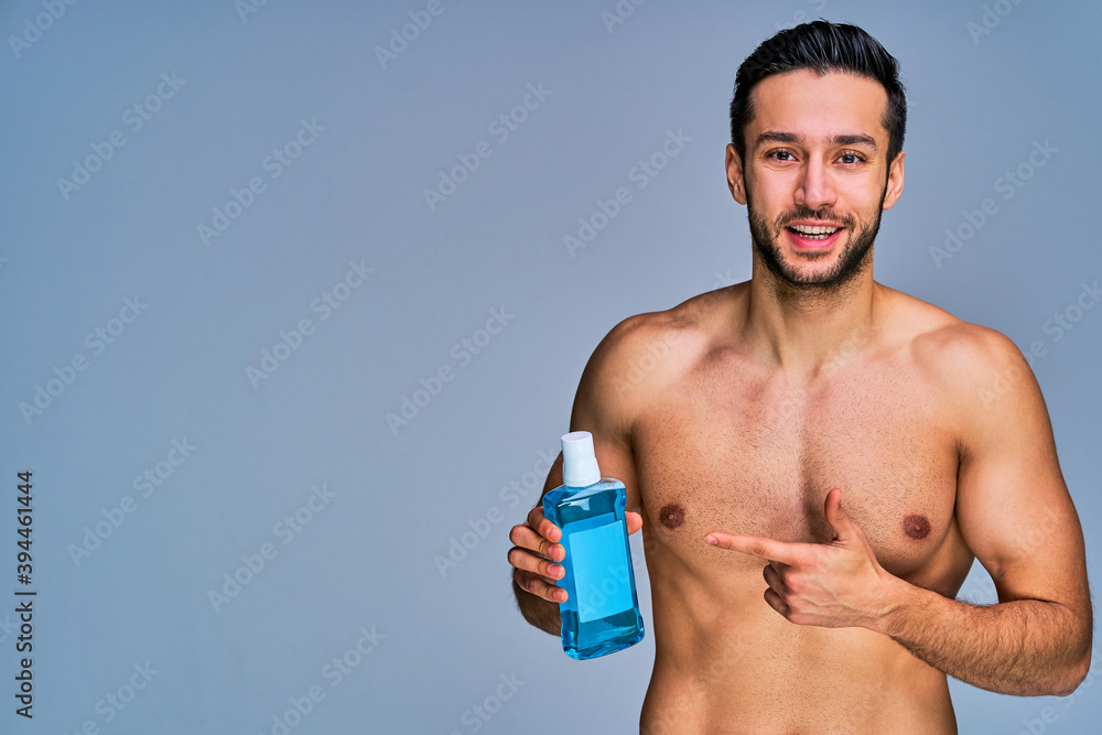 Guy with smile with black hair with a beard offers bottle of mouthwash. Beauty concept Guy with smile with black hair with a beard offers bottle of mouthwash. Beauty concept