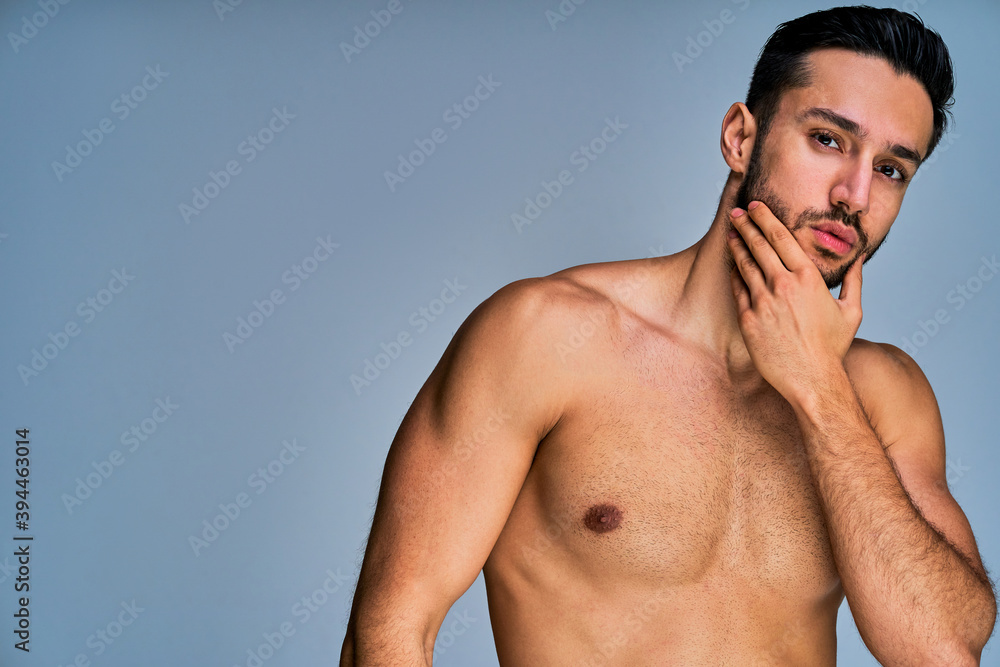Fototapeta premium Tanned man with black hair with a beard examines his face. Beauty concept