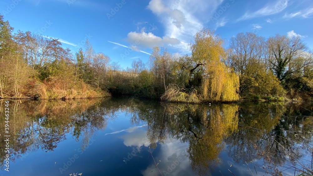 Park canal in a beautiful sunny autumn day with trees and cloud reflecting on the calm, still water, scenic nature landscape, beautiful nature, blue sky and water. Park canal in a beautiful sunny autumn day with trees and cloud reflecting on the calm, still water, scenic nature landscape, beautiful nature, blue sky and water.