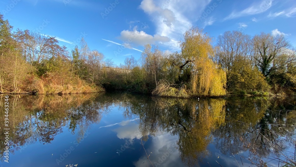 Park canal in a beautiful sunny autumn day with trees and cloud reflecting on the calm, still water, scenic nature landscape, beautiful nature, blue sky and water.