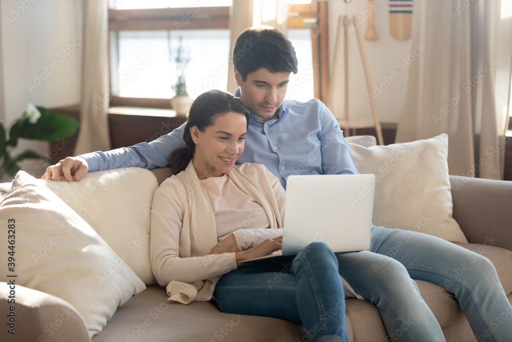 Happy bonding millennial couple in love having date at home embracing on soft comfy couch at living room spending time online using modern laptop pc device watching cute photo video at social networks Happy bonding millennial couple in love having date at home embracing on soft comfy couch at living room spending time online using modern laptop pc device watching cute photo video at social networks